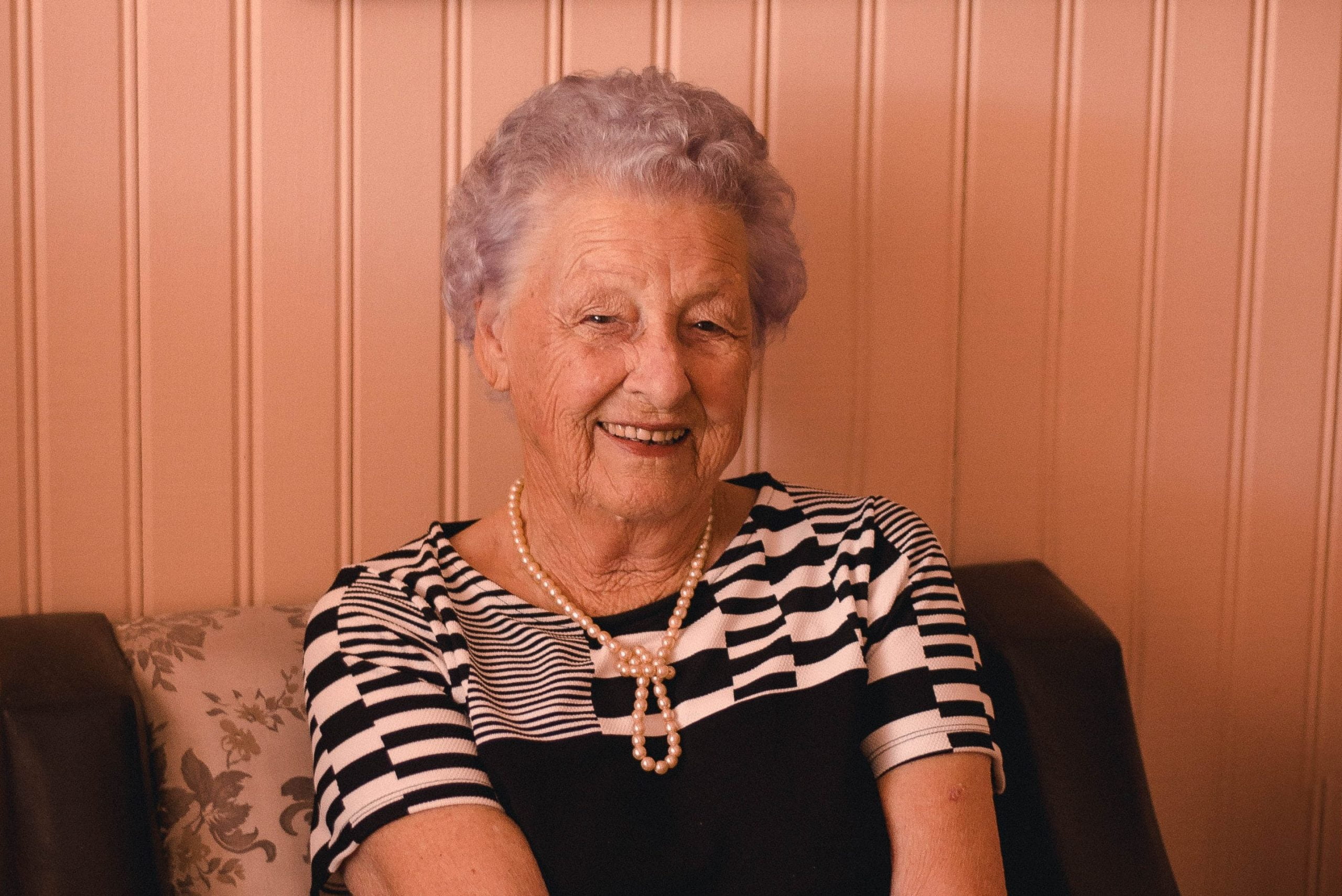 smiling woman wearing black and grey dress sitting on sofa 2269717 4 1024x684 1 scaled